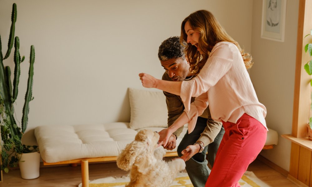 Et par som leker med hunden sin i stuen