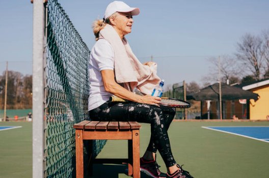 Kvinne med caps som sitter på benk ved en tennisbane