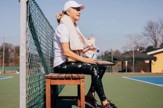 Kvinne med caps som sitter på benk ved en tennisbane Kvinne med caps som sitter på benk ved en tennisbane
