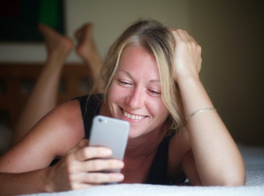 Kvinne ser smilende på mobilen sin.