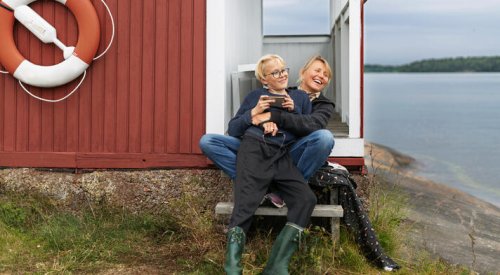Mor og sønn sitter utenfor en hytte ved sjøen. 