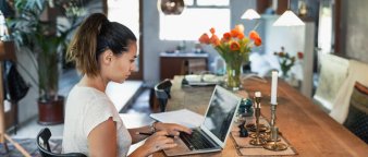Dame som sitter med en PC ved et stuebord. Dame som sitter med en PC ved et stuebord.