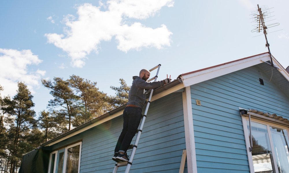 Illustrasjonsfoto: En mann står på en stige mot et blått hus.