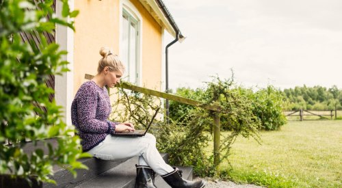 Illustrasjonsbilde: Dame som sitter på trappen utenfor huset sitt og ser på en PC-skjerm.