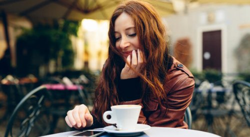 Dame på kafé som drikker kaffe og sjekker mobilen.