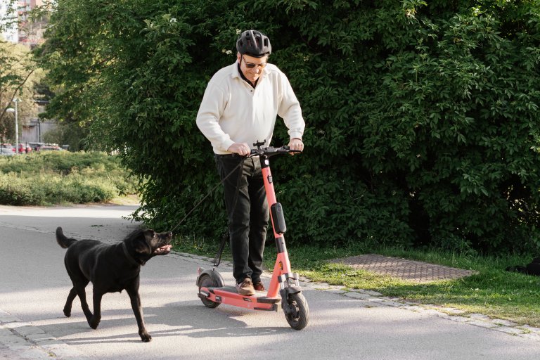 Mann på elsparkesykkel med svart hund.